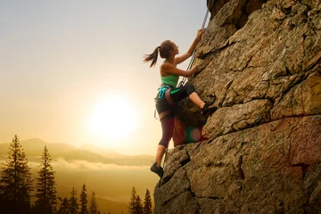 Deurstickers Beautiful Woman Climbing on the Rock at Foggy Sunset in the Mountains. Adventure and Extreme Sport Concept © Maksym Protsenko