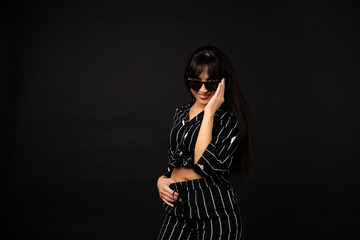 Young business girl in a black suit posing for a photo on a black background.