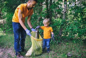 Volunteers activists picking up litter in the park. Father and his toddler son cleaning up forest...
