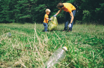 Father and son picking up plastic garbage for cleaning park. Volunteers tidying up rubbish in the forest. Concept of environmental protection