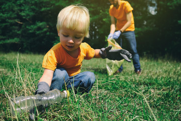 Volunteers activists child and his father in gloves tidying up rubbish in park or forest. Save...