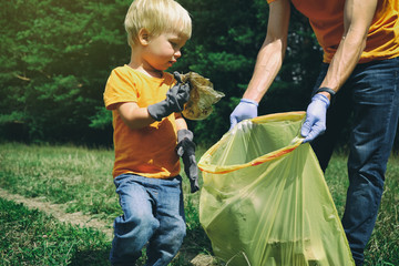 Cute toddler boy and his father collecting garbage in the park. Volunteers family picking up litter...