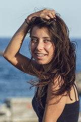 Close-up portrait of cheerful suntanned young woman over seaside background. Vertical shot of beautiful brunette girl relaxing on the resort under the hot sun.