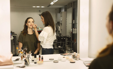 Professional Makeup Artist Applying Eyeshadow To Young Woman In Salon