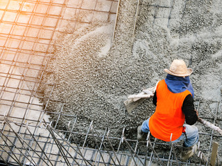 Top view of builders in orange shirt pouring concrete works on the construction site