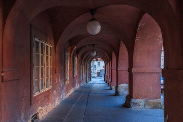 Long arched house in red with lamps on the ceiling. Granite floor panels and pedestal. Historic windows on the wall without people in Prague from Hradcany square