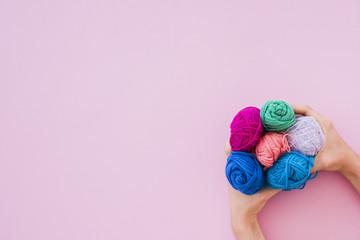 An elevated view of hand holding colorful wool on pink background