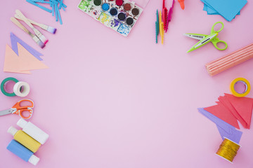 Paintbrush; color palette; scissor; golden spool; paper and scissor on pink backdrop
