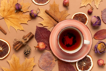 Autumn Flat lay composition. Cup of tea, autumn dry bright leaves, roses flowers, orange circle, cones, decorative pomegranate, cinnamon sticks on brown beige background top view. Autumn, fall concept