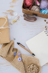 Buttons; wrapped gift box; measuring tape; pen; knitted scarf and spiral notepad on white wooden table