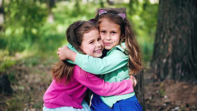 Two smiling, cute young girls hug each other tightly against the background of beautiful nature. True friendship, friends for ages. Positive emotions, laughter and love.