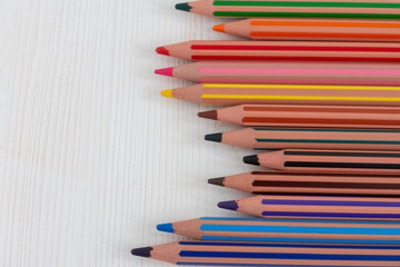Top view of colored pencils for school, horizontally, on white wooden background with copy space