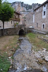 Fototapeta na wymiar Stream Leaving Through A Bridge In The Middle Of The Streets In Orbaneja Del Castillo. August 28, 2013. Orbaneja Del Castillo, Burgos, Castilla Leon, Spain. Vacation Nature Street Photography.