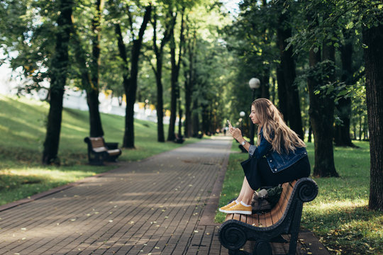 lonely woman waiting at park, entertaining with her smartphone.