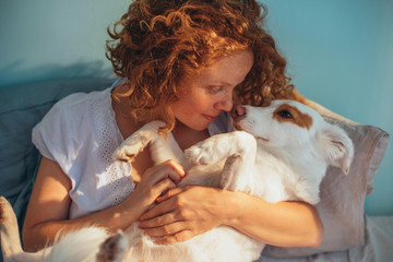 Young woman cuddling with her dog on bed