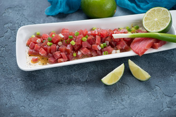Tuna ceviche served in a white plate over blue stone background, horizontal shot with copy space