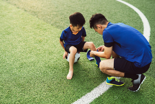 Father putting socks on his son on soccer field