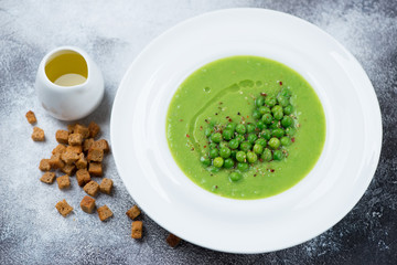 Green peas cream-soup served in a white plate with croutons and olive oil, horizontal shot on a light grey stone background