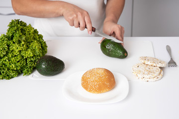 The girl is holding an avocado. Woman cutting fresh avocado at table. Breakfast of avocado.