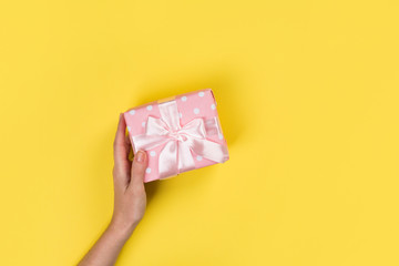 Womans hands holding gift or present box on Yellow table top view. Flat lay  for birthday or New Year. Top view