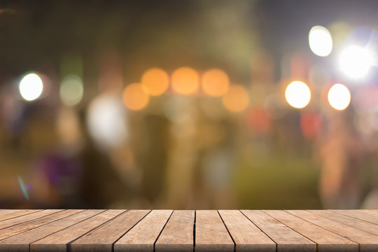 Blurred wooden table in front blurred night street market with bokeh abstract background, copy space for presentation product