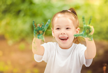 a little cheerful girl draws with finger paints in the fresh air