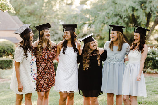 Graduate women in dresses and caps standing outdoors