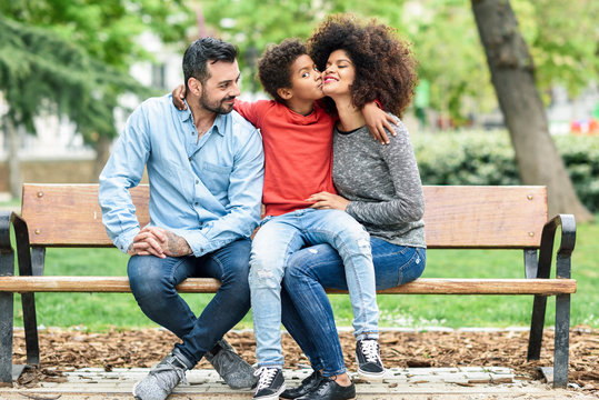 Family sitting on a park bench, son kissing mother