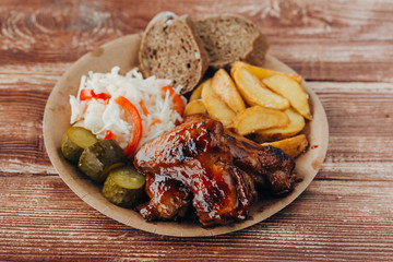 Delicious fried chicken wings with sauce, fried potatoes, cucumber, cabbage and khlobe in a paper plate on a wooden table. takeaway street food