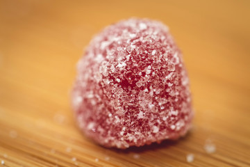 A macro portrait of a sugar sprinkled red piece of candy on a wooden table. There is suger sprinkled around it as well.