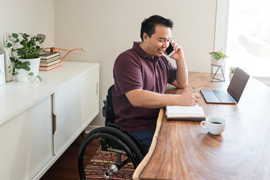 Asian man in wheelchair talking on cell phone.