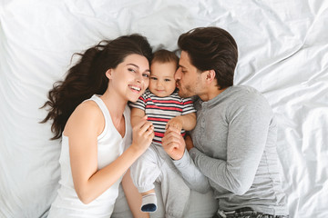 Positive young parents enjoying happy morning with adorable baby