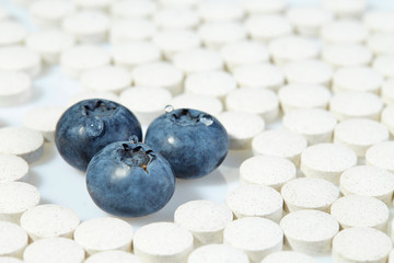 Three ripe blueberries are surrounded by pills on all sides. Concept: natural vitamins.