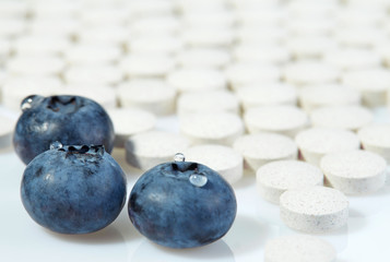 Three ripe blueberries on a background of tablets spread out on a light surface. Concept: natural vitamins.