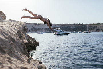 Young beautiful woman jumping in the sea from the rock