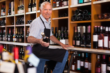 Positive male vintner holding out bottle of wine