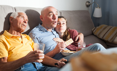 Woman with husband and father  watching tv on sofa at home