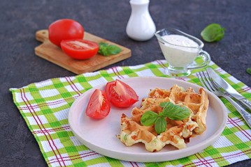 Savory zucchini waffles on a white plate on a dark concrete background. Served with ranch dressing and fresh tomato. Healthy food.