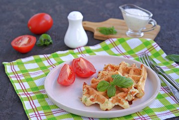 Savory zucchini waffles on a white plate on a dark concrete background. Served with ranch dressing and fresh tomato. Healthy food.