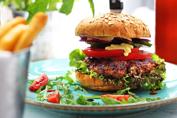 Burger with a grilled beef cutlet, tomato, cucumber, lettuce and sauce served on a plate.
