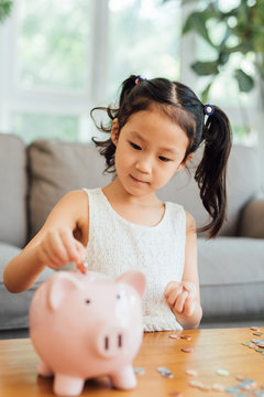 Chinese girl putting coins into piggy bank