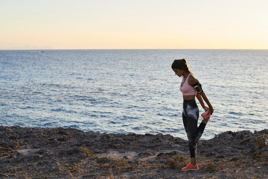 Pensive runner stretching at sunset in front of sea.