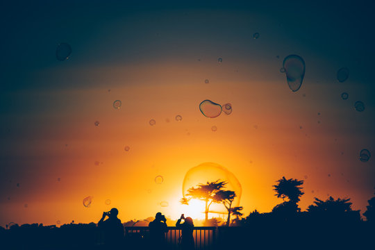 People taking photos of large bubbles at sunset
