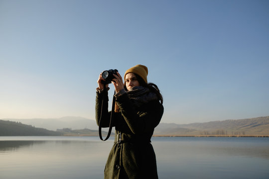 Young woman taking picture with digital camera by lake