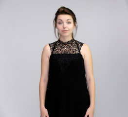 A portrait above the knee of a pretty beautiful fashionable adult brunette girl in a black dress on a white background. Standing right in front of the camera, showing different poses and emotions.