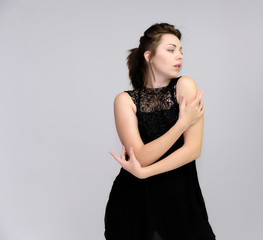 A portrait above the knee of a pretty beautiful fashionable adult brunette girl in a black dress on a white background. Standing right in front of the camera, showing different poses and emotions.