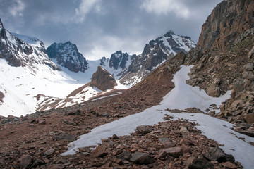 Fototapeta na wymiar Panorama of the Trans-Ili Alatau mountain range of the Tien Shan system in Kazakhstan near the city of Almaty. Rocky peaks covered with snow and glaciers in the middle of summer under clouds