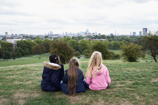 Faceless girl friends sitting at park with views.