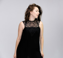 Fototapeta premium A portrait above the knee of a pretty beautiful fashionable adult brunette girl in a black dress on a white background. Standing right in front of the camera, showing different poses and emotions.
