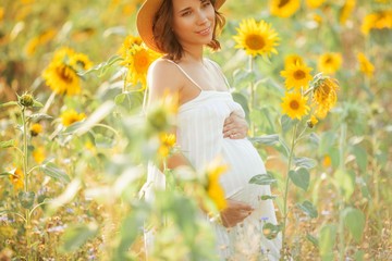 Beautiful young pregnant woman in the sunflower field. Portrait of a young pregnant woman in the sun. Summer.